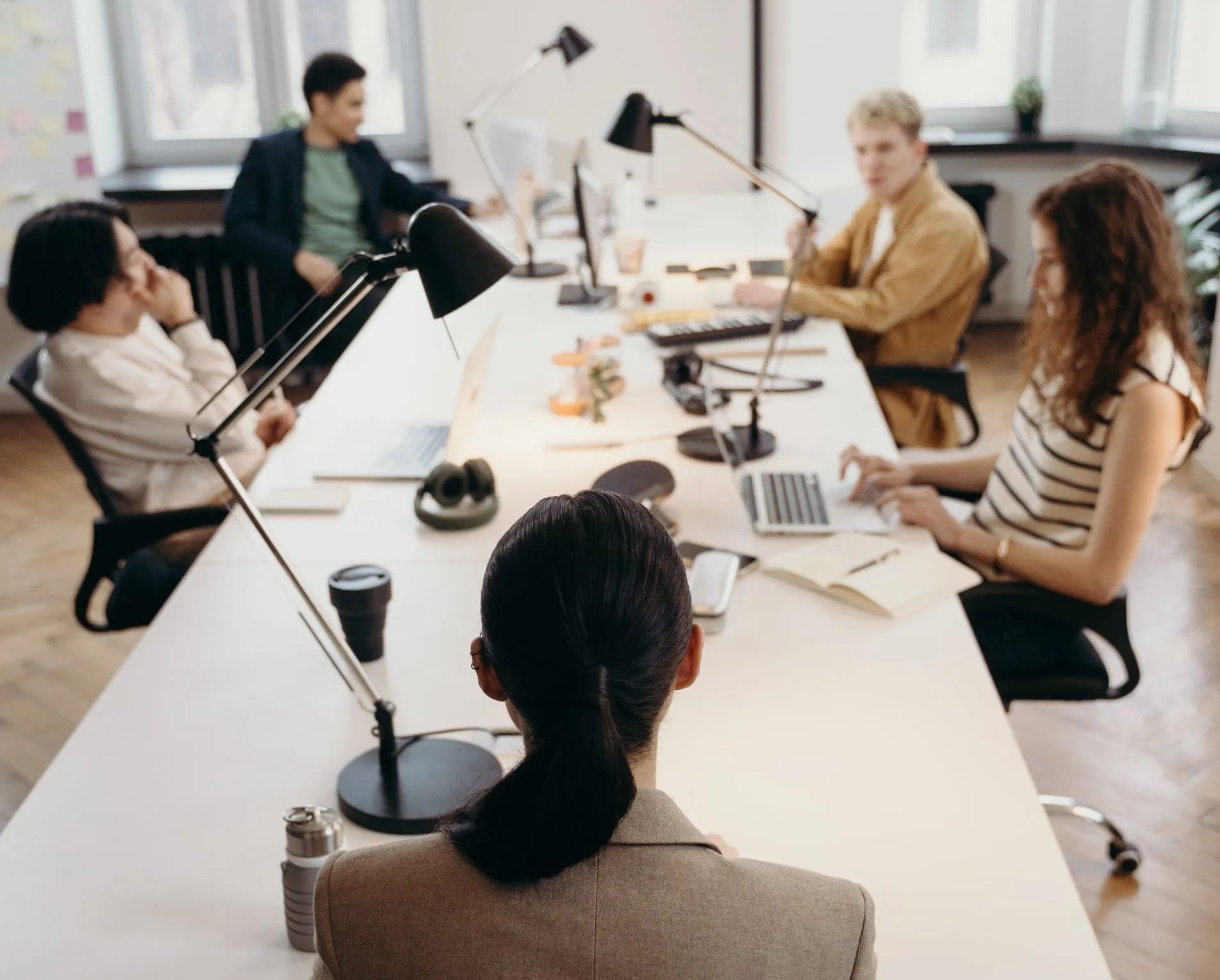 A group of people are sitting around a long table with laptops.