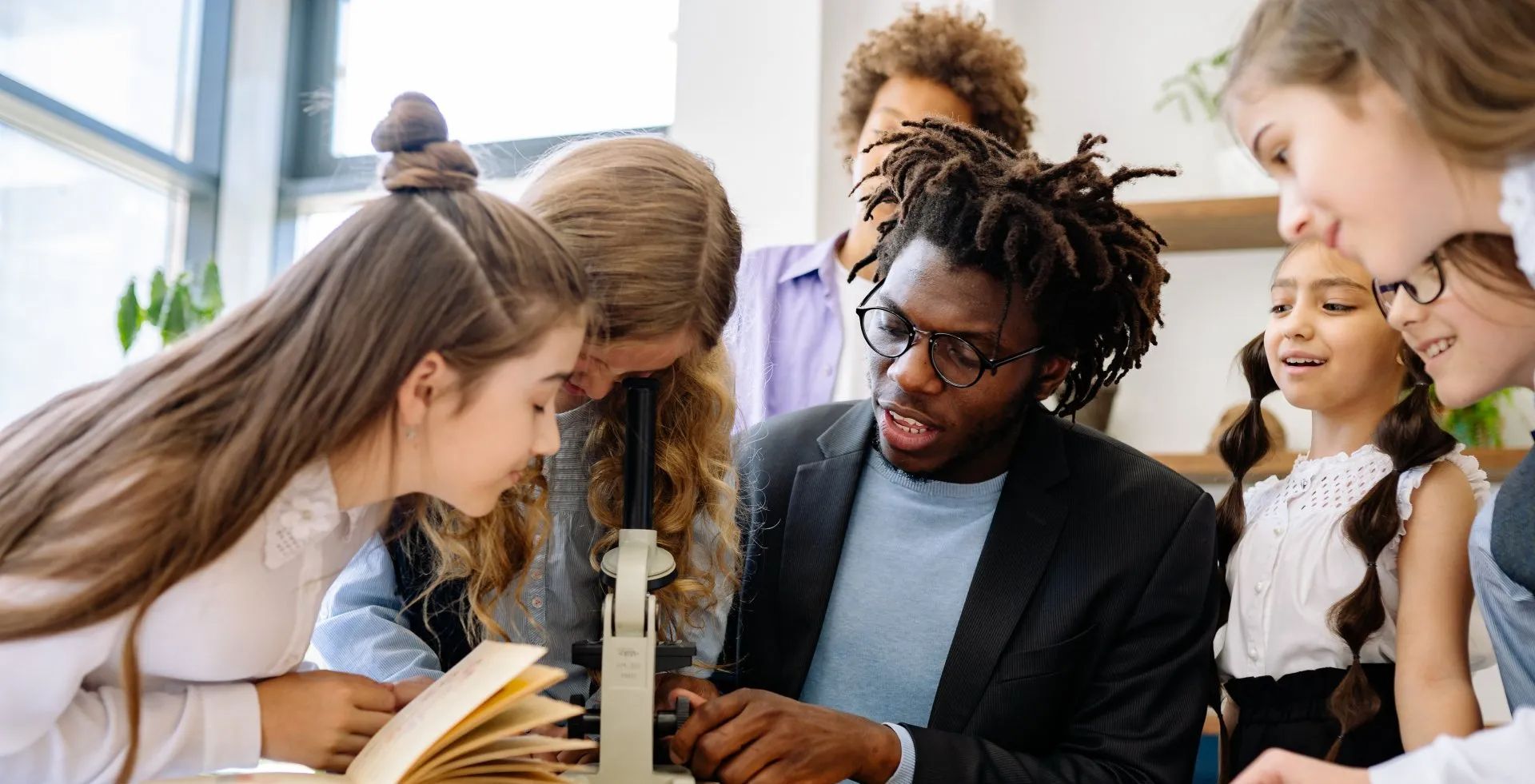 A man is teaching a group of children how to use a microscope.