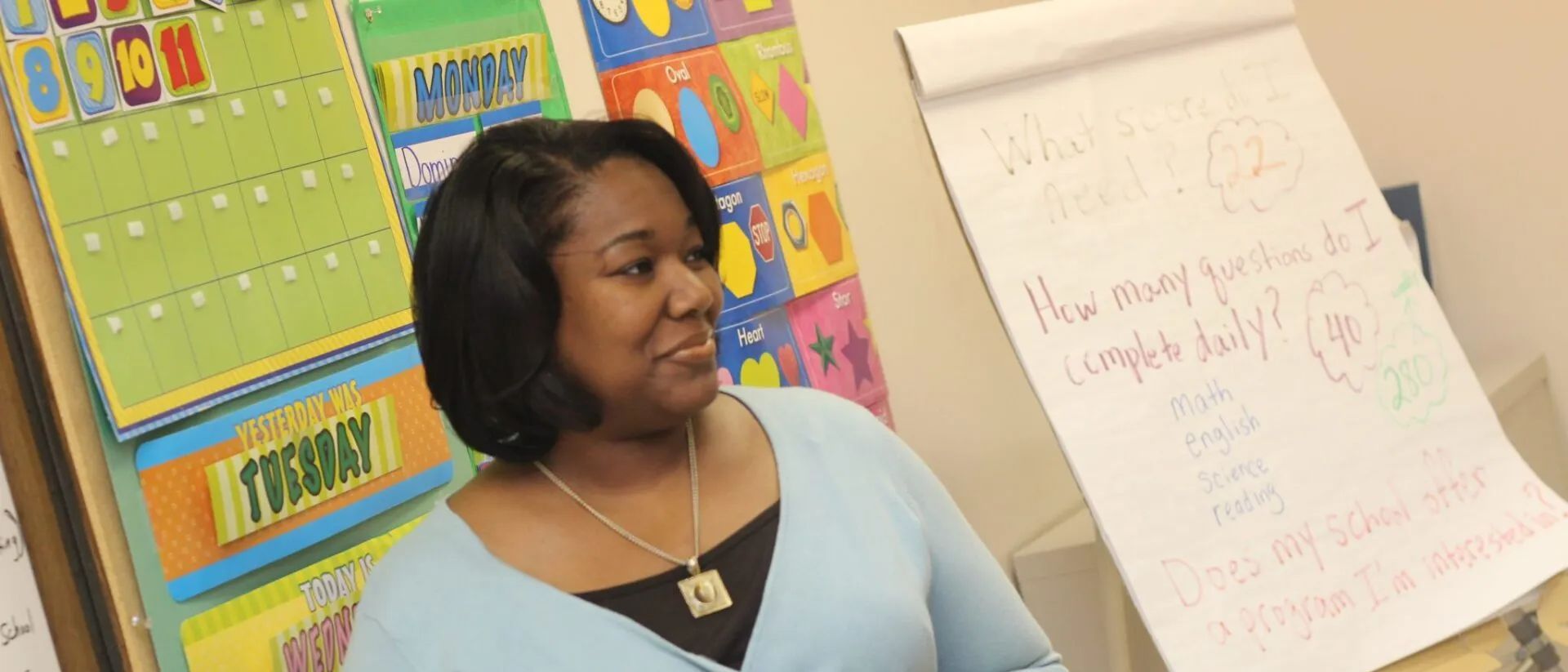 A woman in a blue shirt is standing in front of a white board.