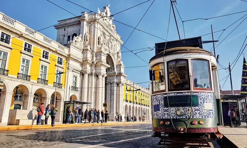 A yellow tram passing the arcades of Praça do Comércio in Lisbon