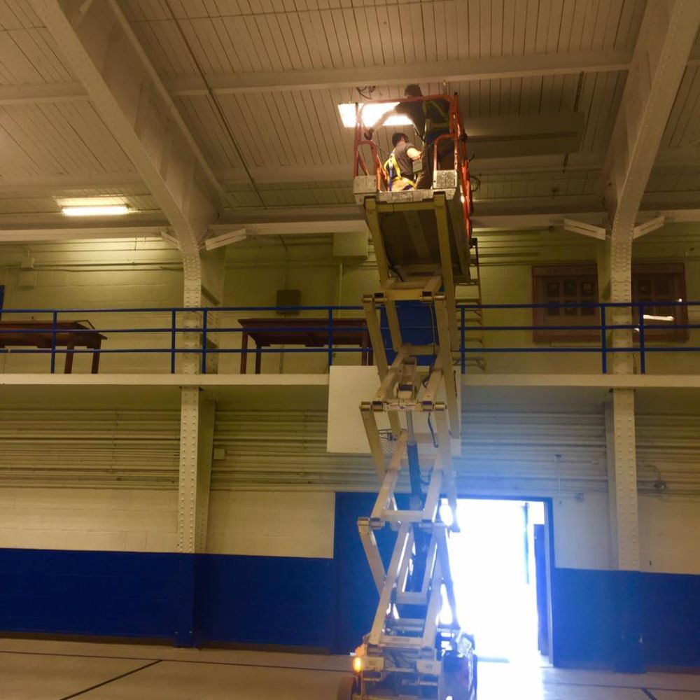 A man is standing on a scissor lift in a gym