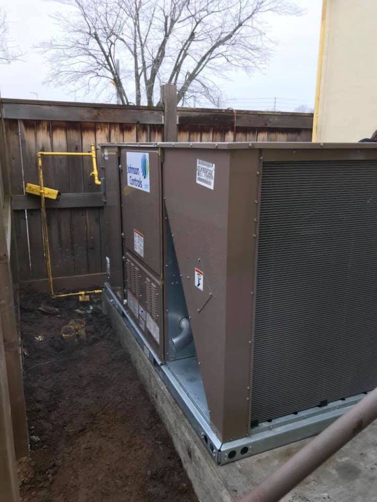 A large brown box is sitting in the dirt next to a wooden fence.