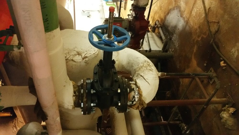 A blue valve is sitting on top of a pipe in a room.