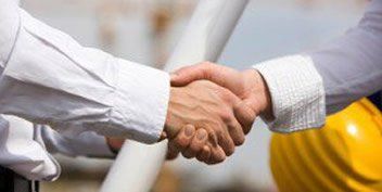 Two men are shaking hands in front of a yellow hard hat.