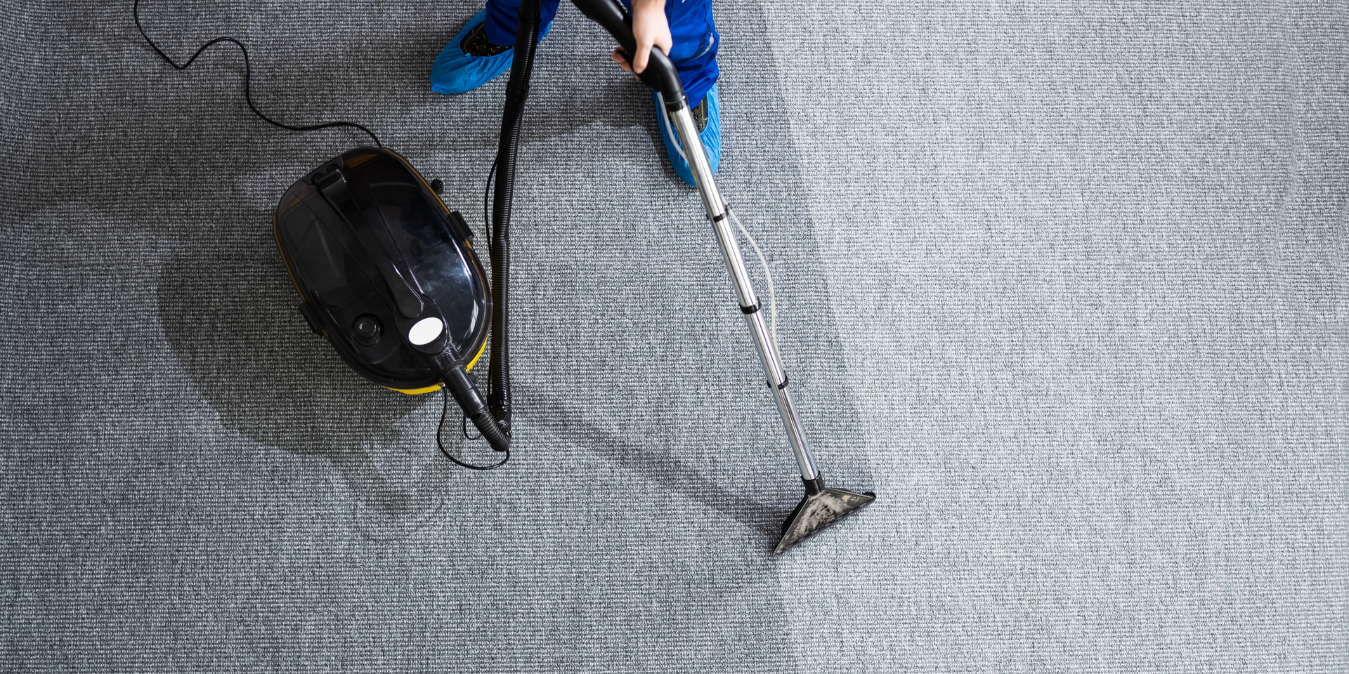 Person using a carpet cleaner on a grey rug, with a cleaned area visible.