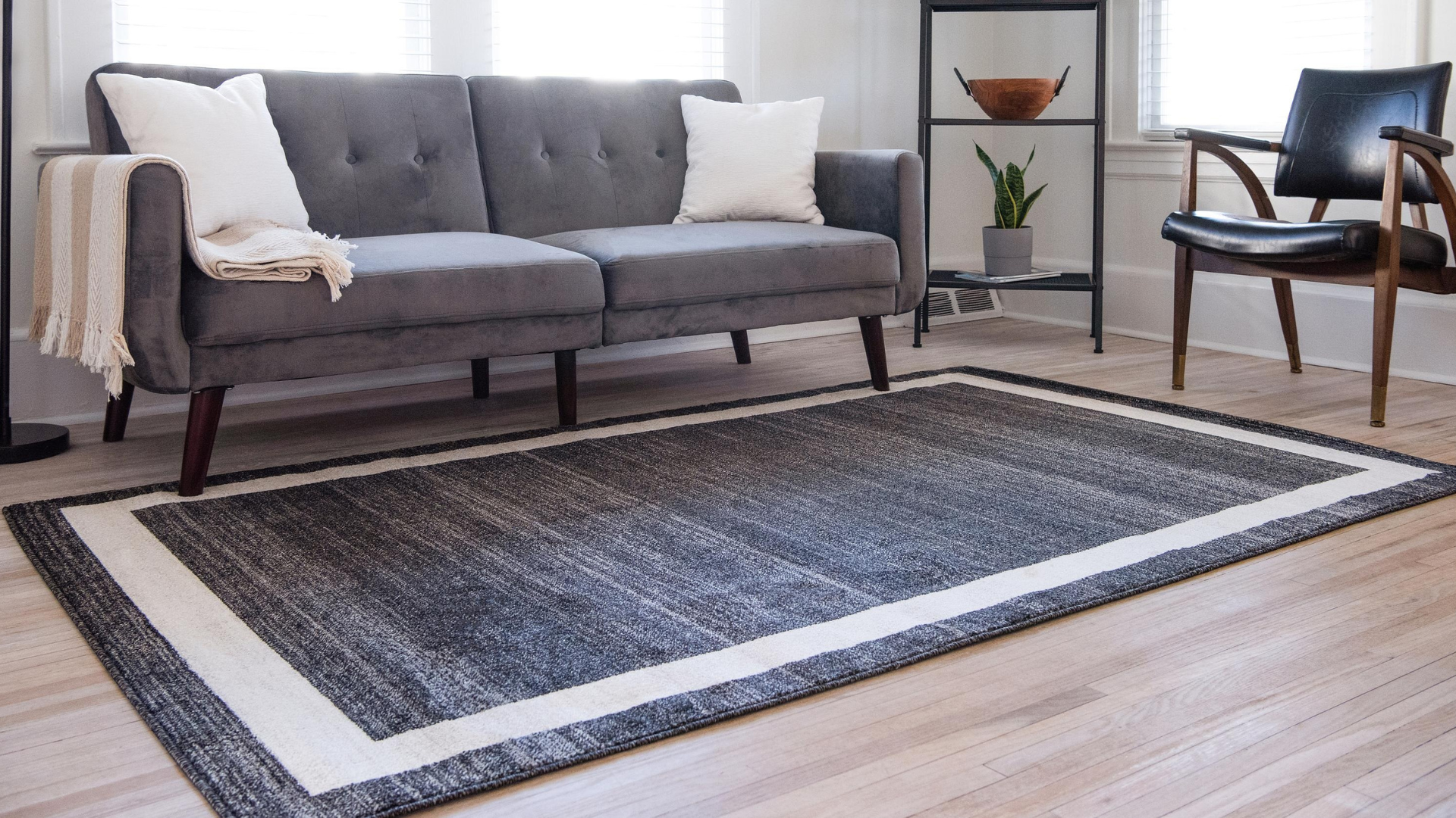 Gray sofa in a living room on a rectangular rug with a white border.