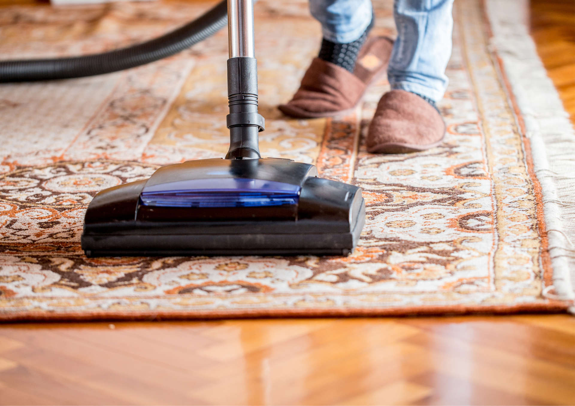 Vacuum cleaner cleaning a patterned rug on a wooden floor.