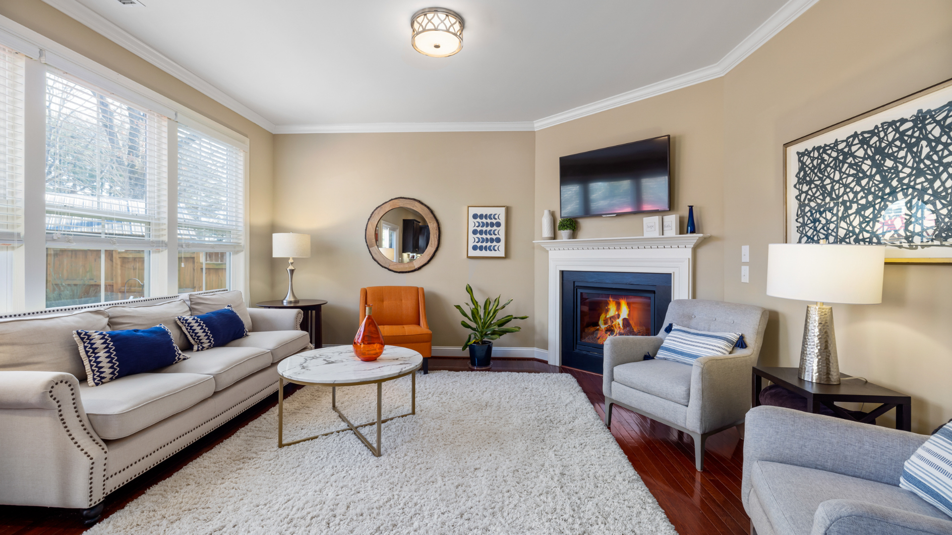 Living room with fireplace, sofa, chairs, area rug, and artwork. Warm, neutral color palette.