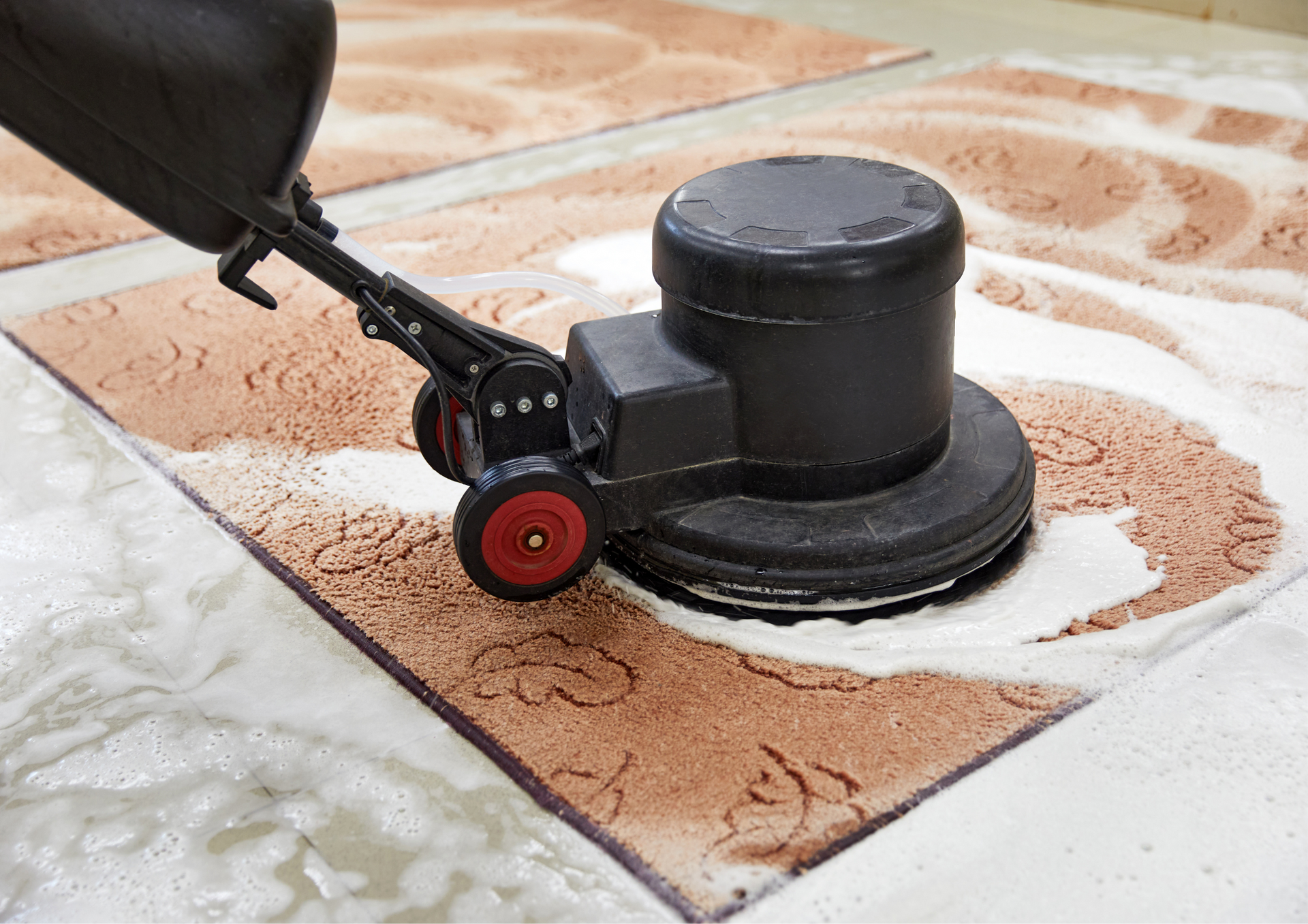 Carpet cleaner scrubbing a brown rug, surrounded by soapy water, on a tiled floor.