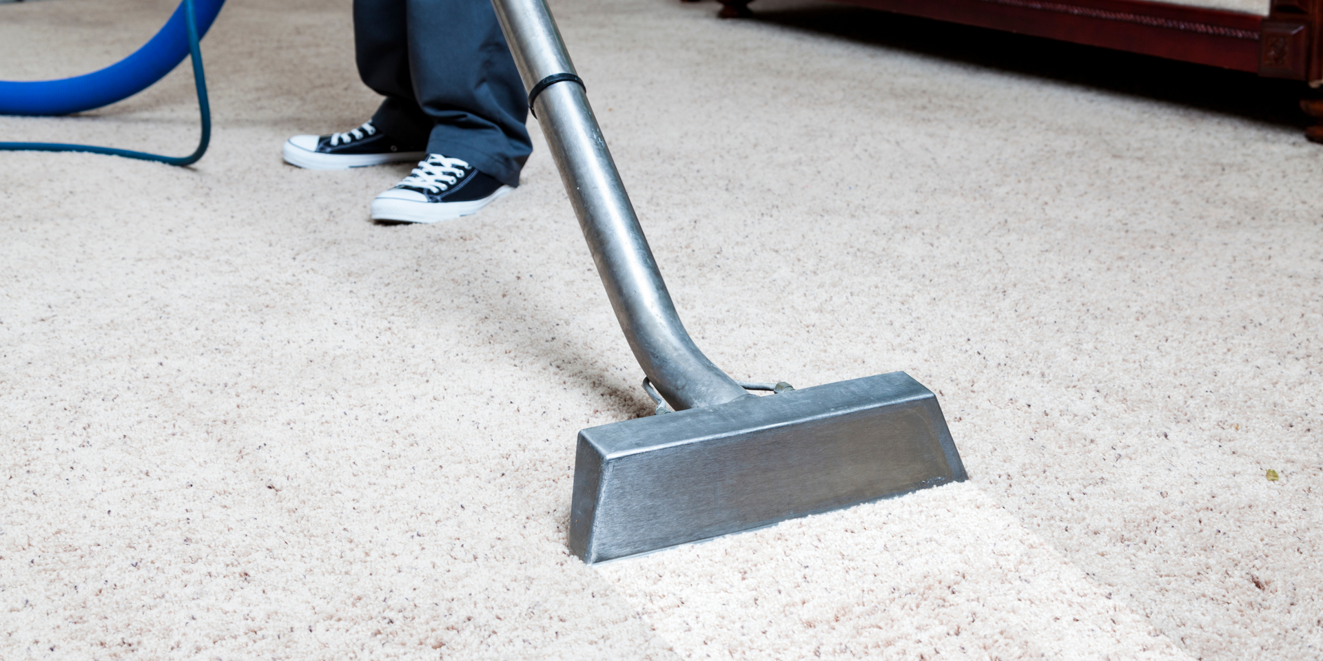 A person cleans a carpet with a vacuum machine, leaving a clean path.