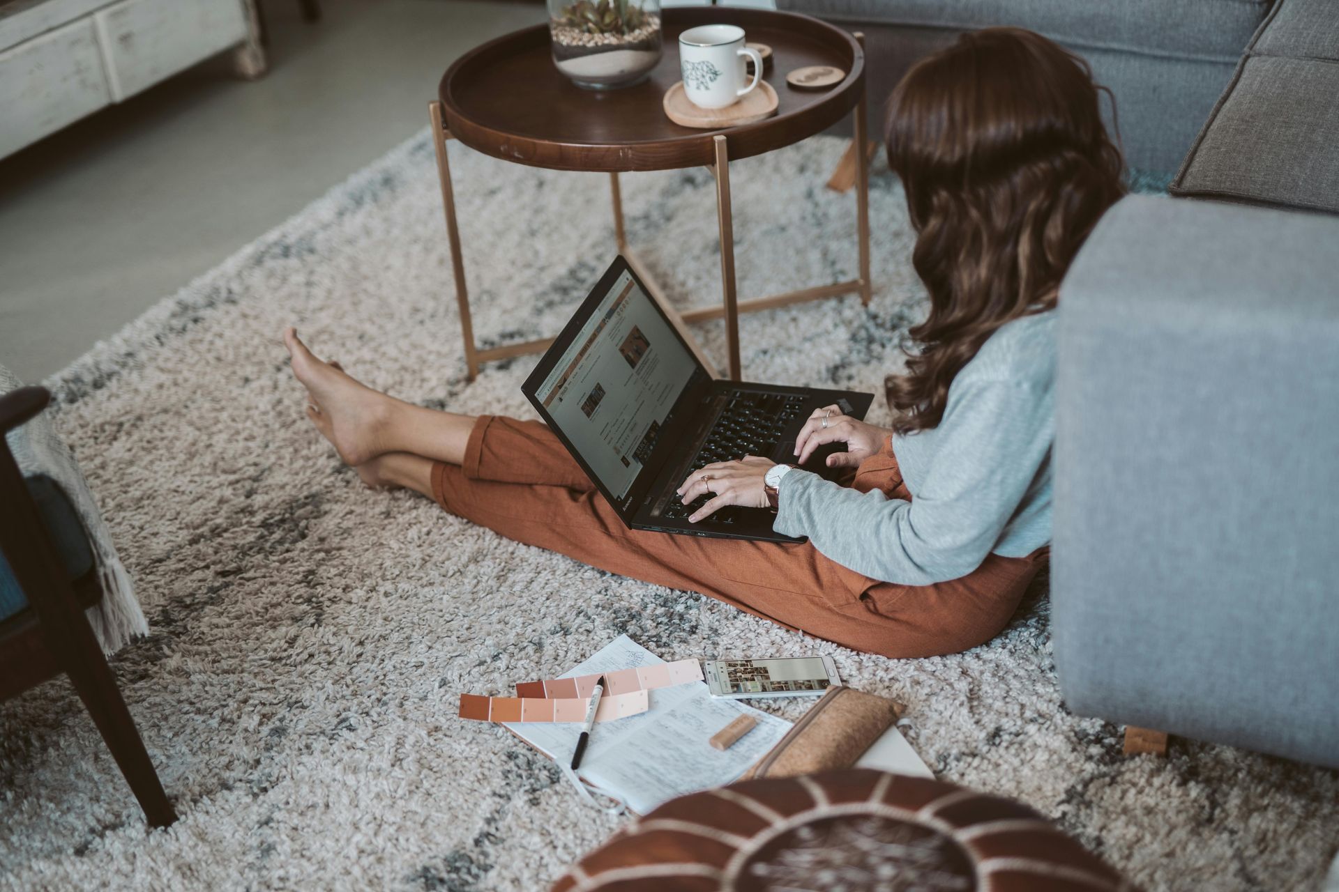 Woman working on laptop on the floor; small table with coffee cup nearby.