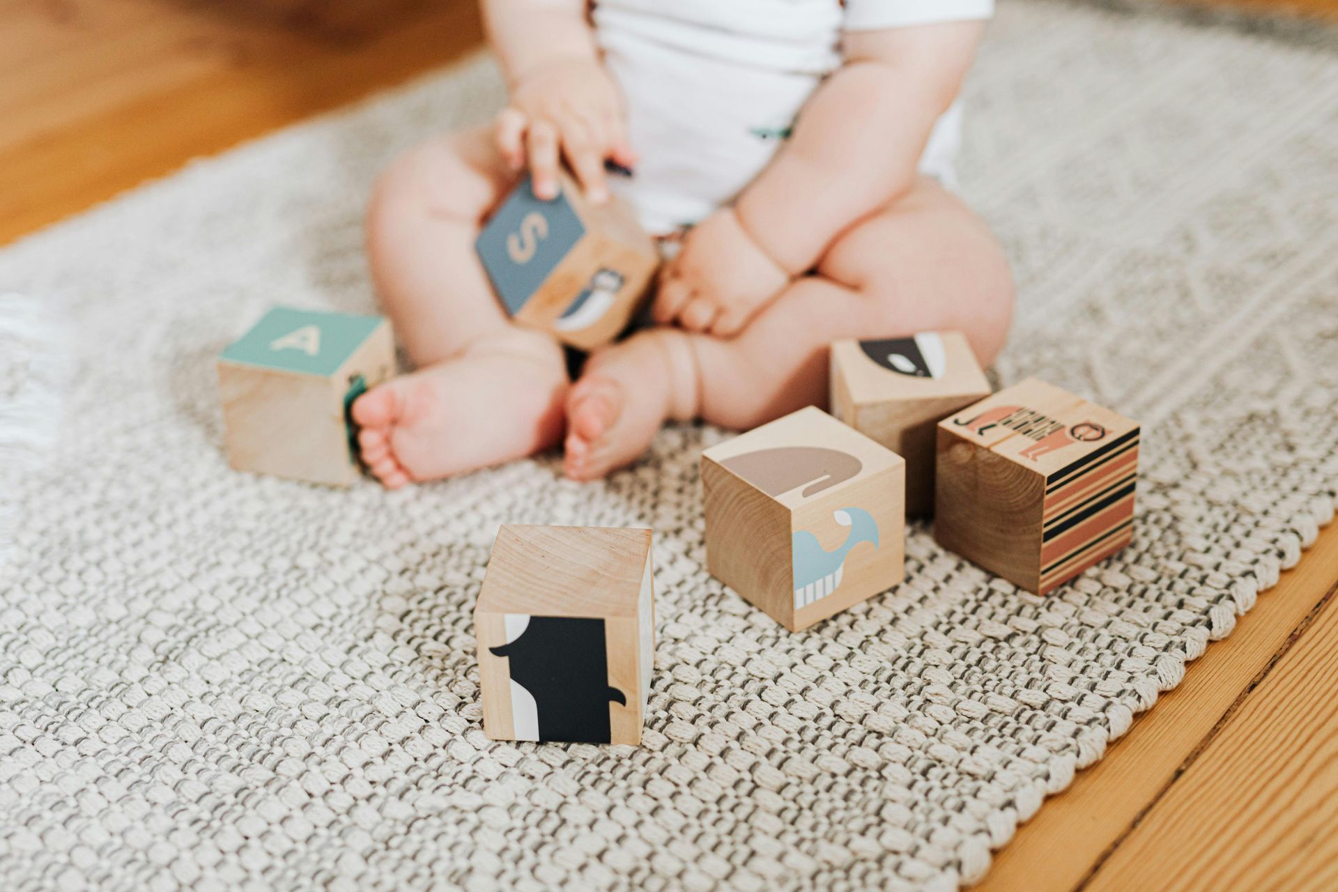 Baby playing with wooden blocks on a rug.