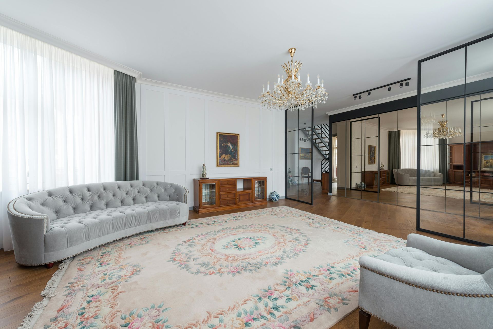 Elegant living room with curved sofa, ornate rug, and chandelier.
