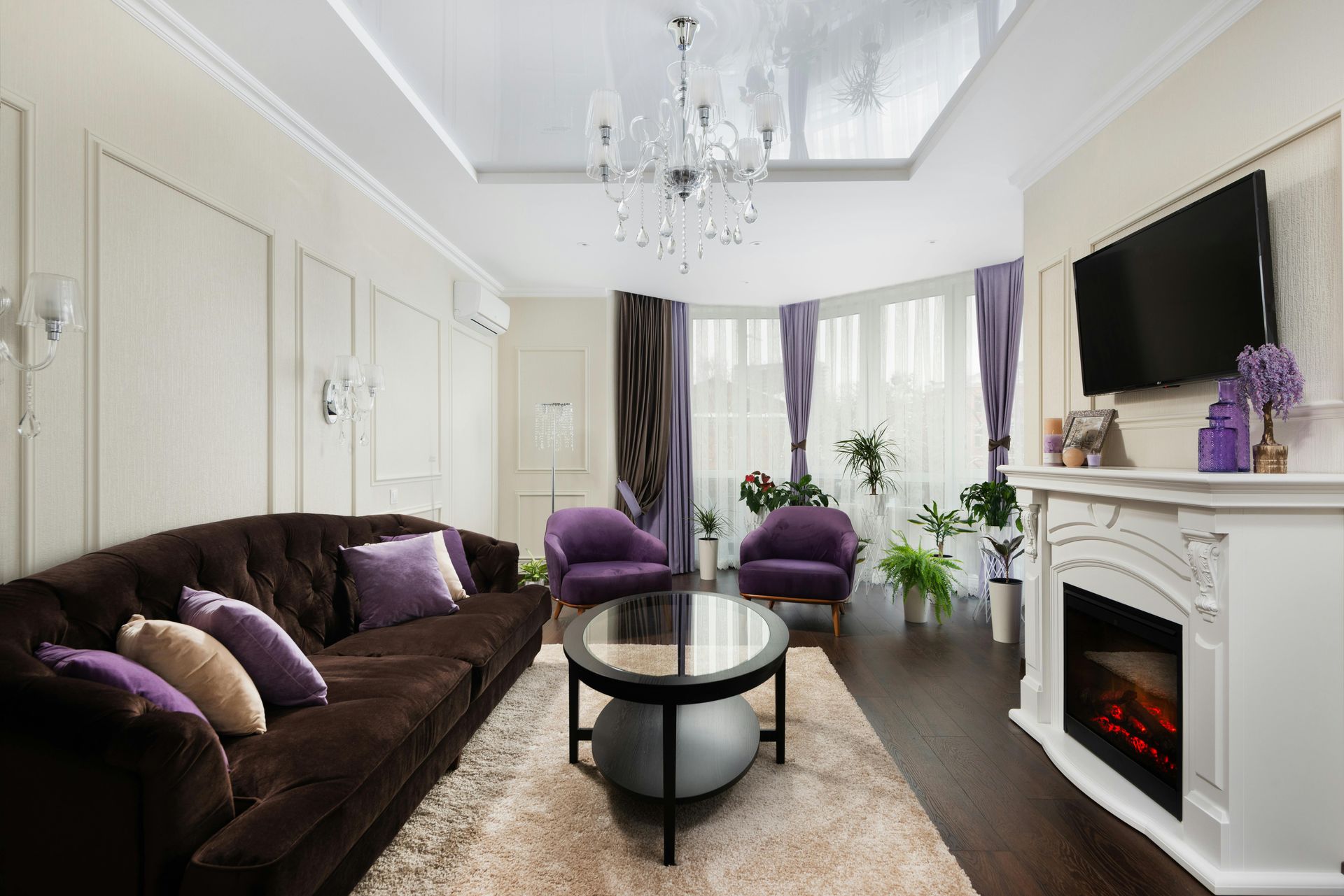 Living room with brown sofa, purple armchairs, fireplace, TV, and chandelier.