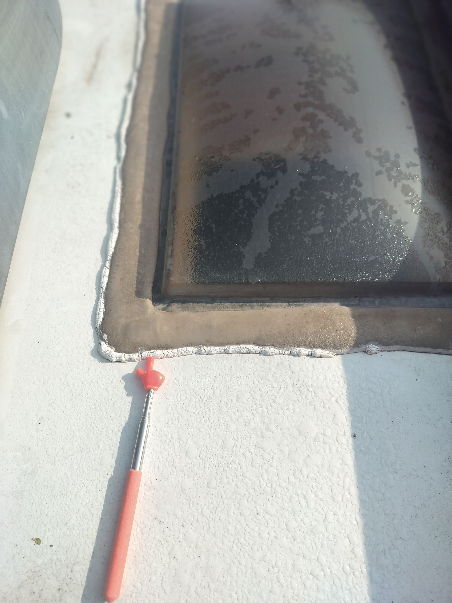 Close-up of a white wall corner with a dark window and a red cable or pipe running down the side