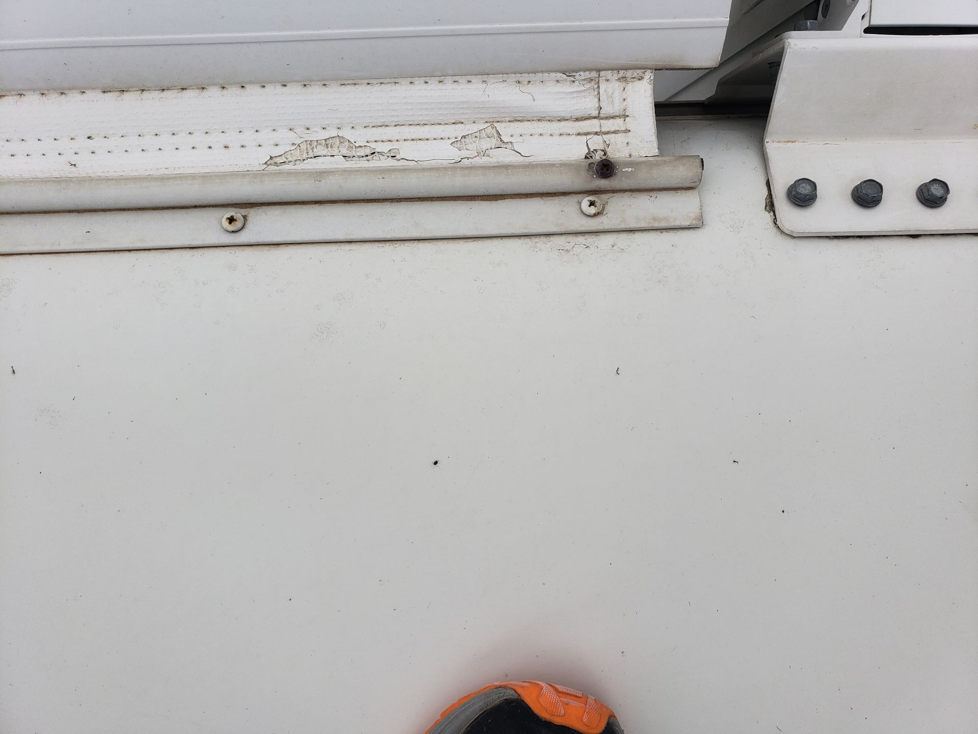 White trailer exterior with a section of trim and screws visible, alongside the edge of a door.