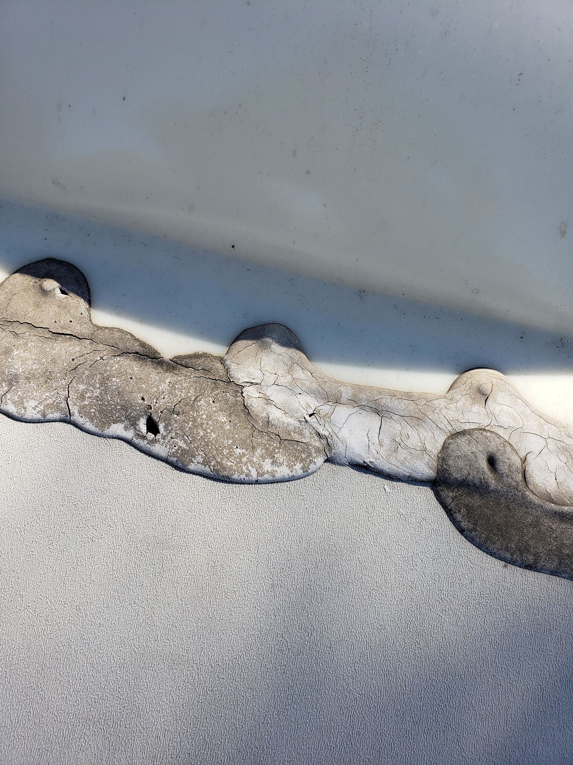 Close-up of damaged roof edge with eroded, grayish coating and small holes.