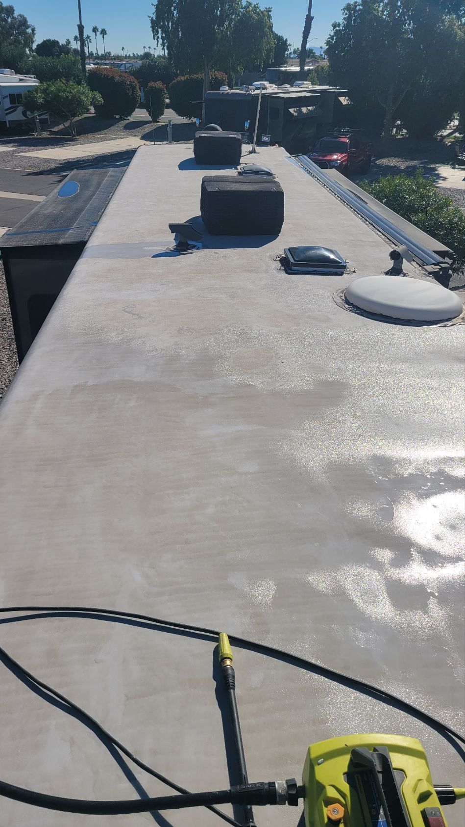 Sunlit flat RV rooftop with vents and pipes, viewed from a maintenance cart at the edge.