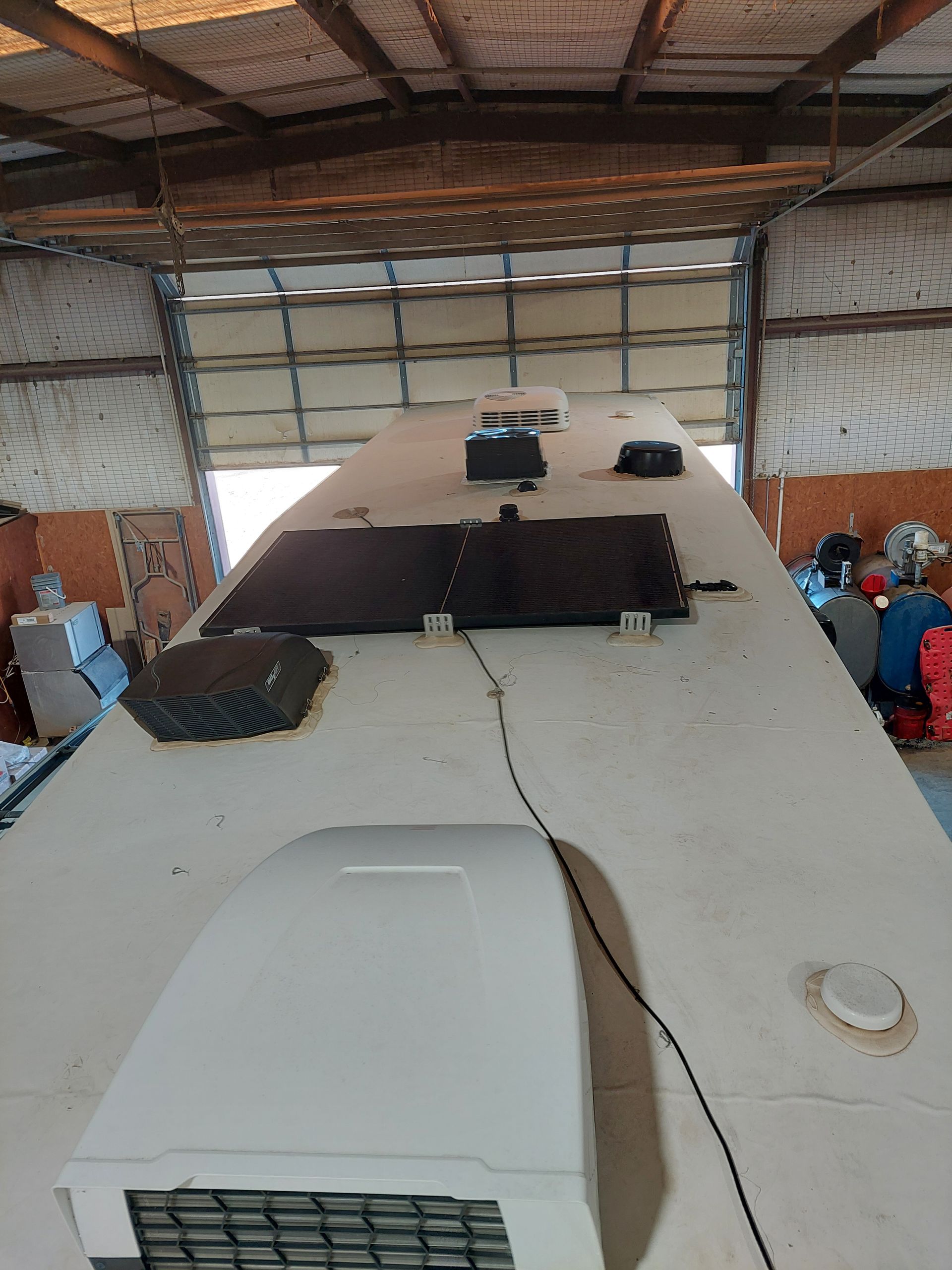 Inside a warehouse, a large white RV sits under construction with tools and workers around it