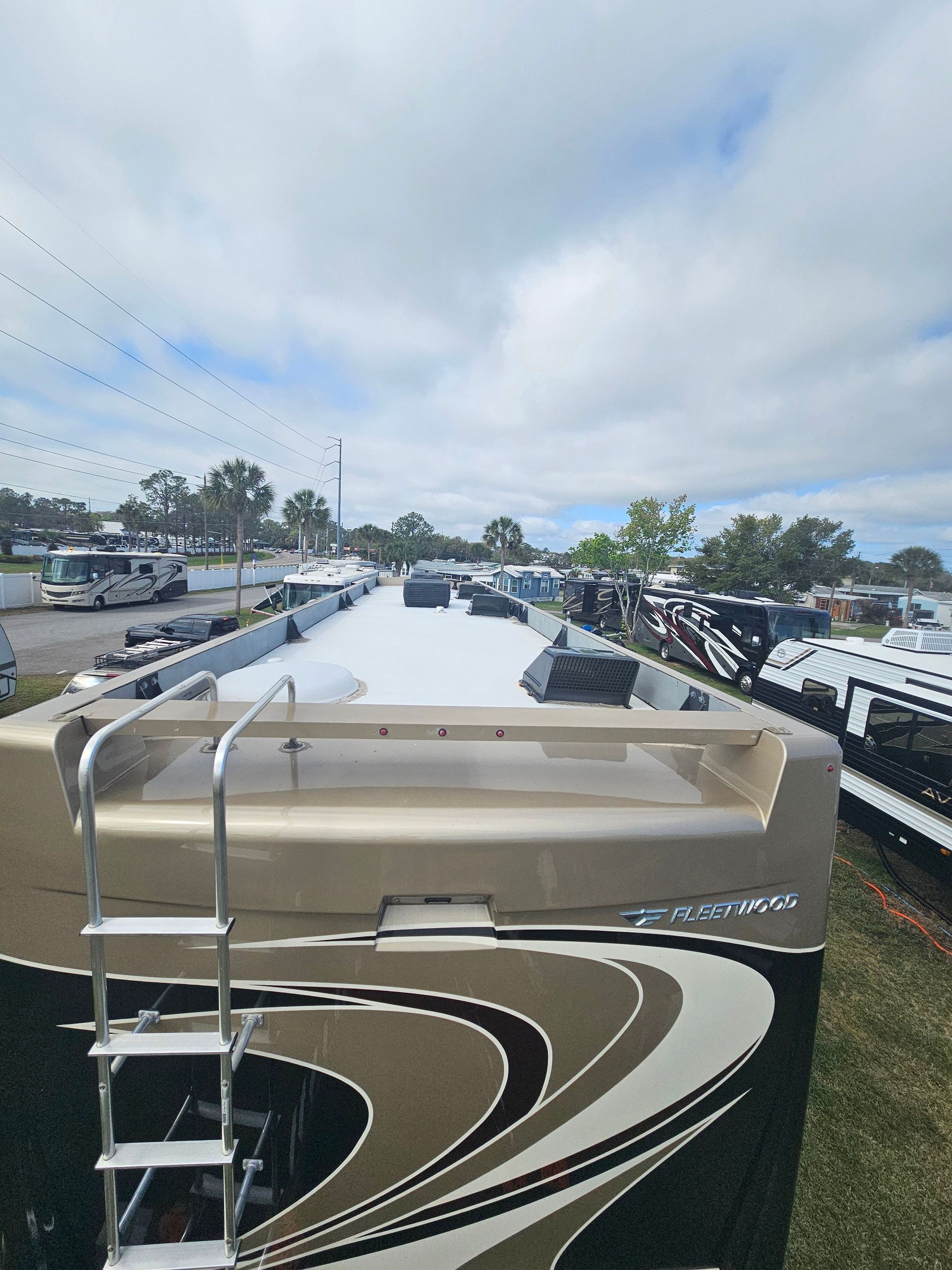 Luxury RV parked in a lot, rear view with ladder and black-and-white swirl graphics