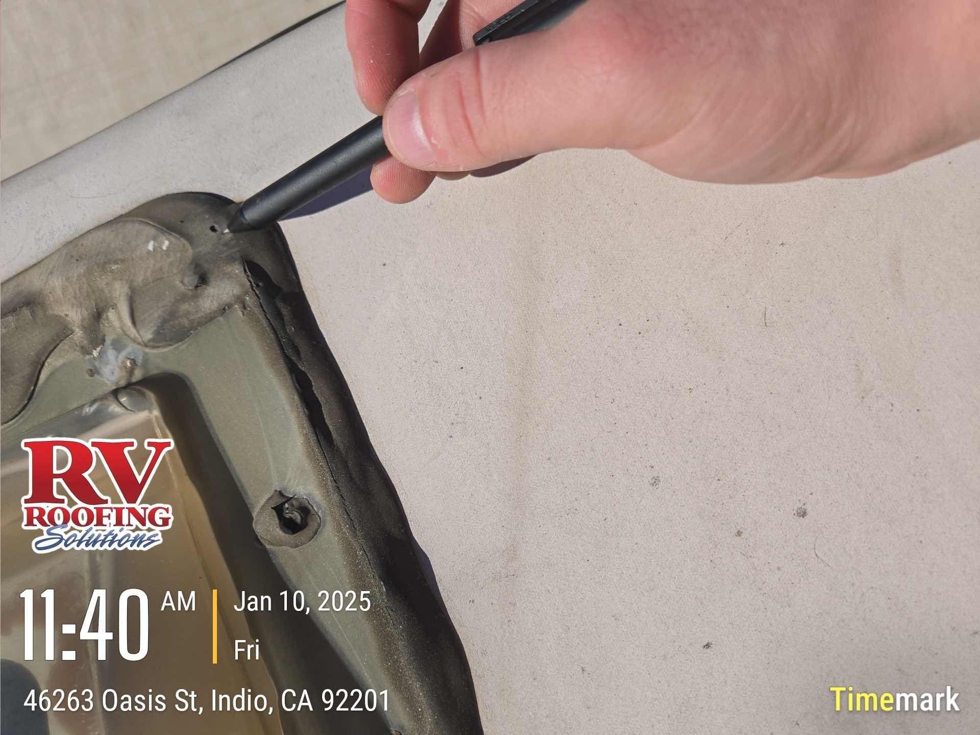 Hand with pen pointing at damaged RV roof seam, near a vent