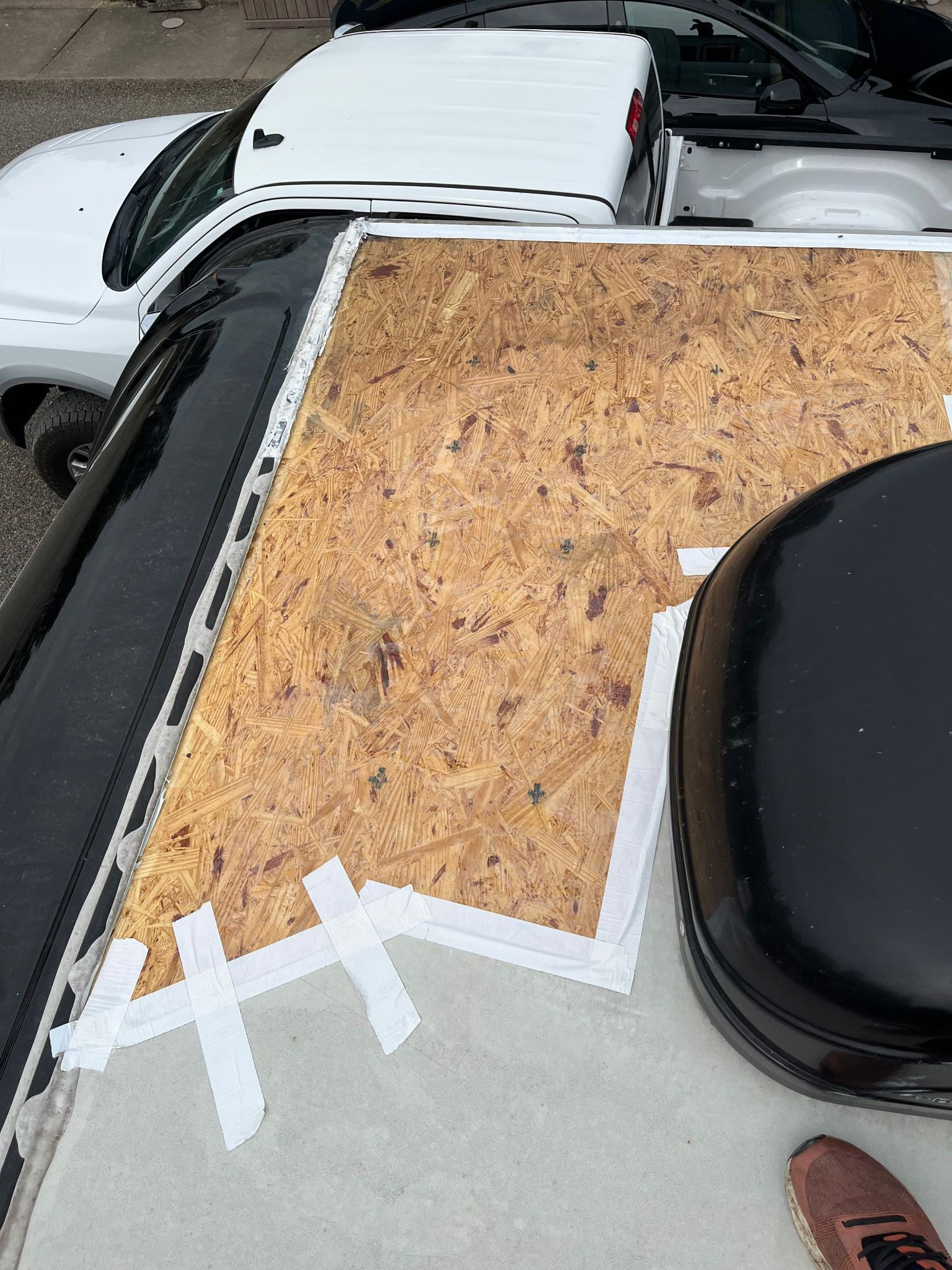 A partially repaired RV roof with exposed OSB, white tape, and a black vent. A white truck is in the background.