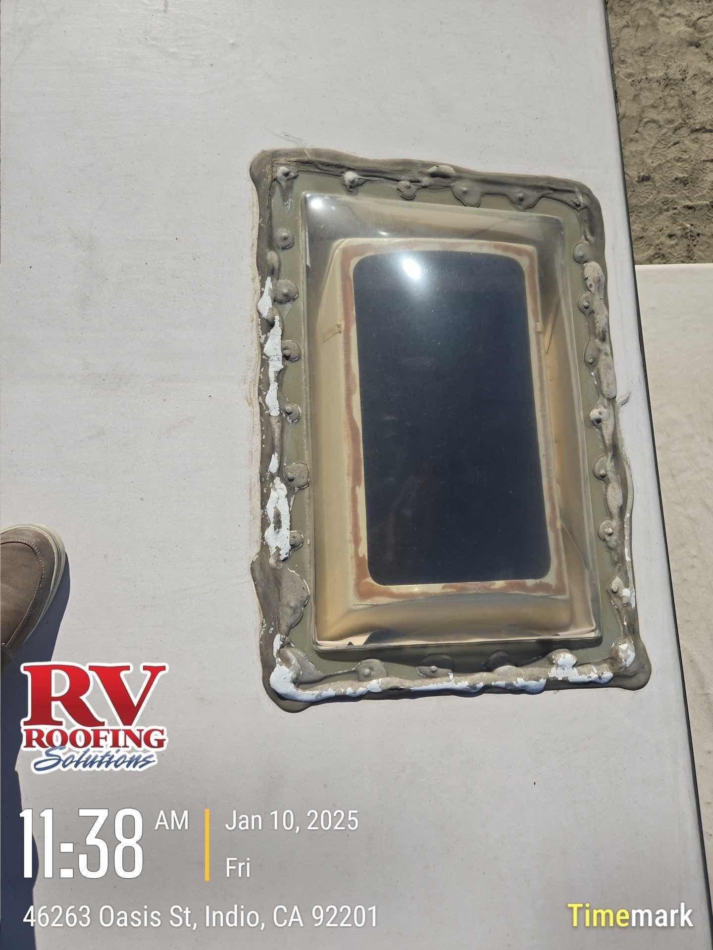 RV roof vent with dark tinted window, sealed with gray caulk on a white surface.