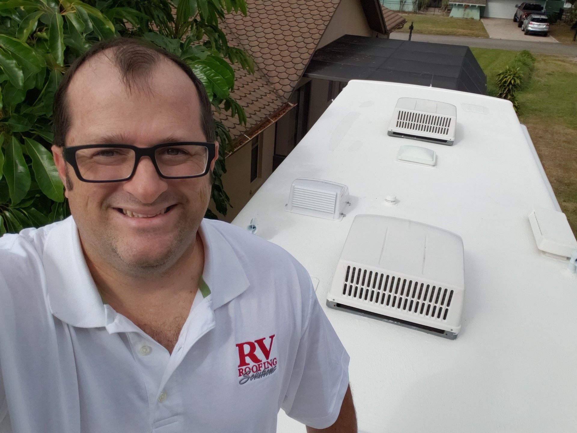 A man wearing glasses is standing on top of an RV Roof done by RV Roofing Solutions