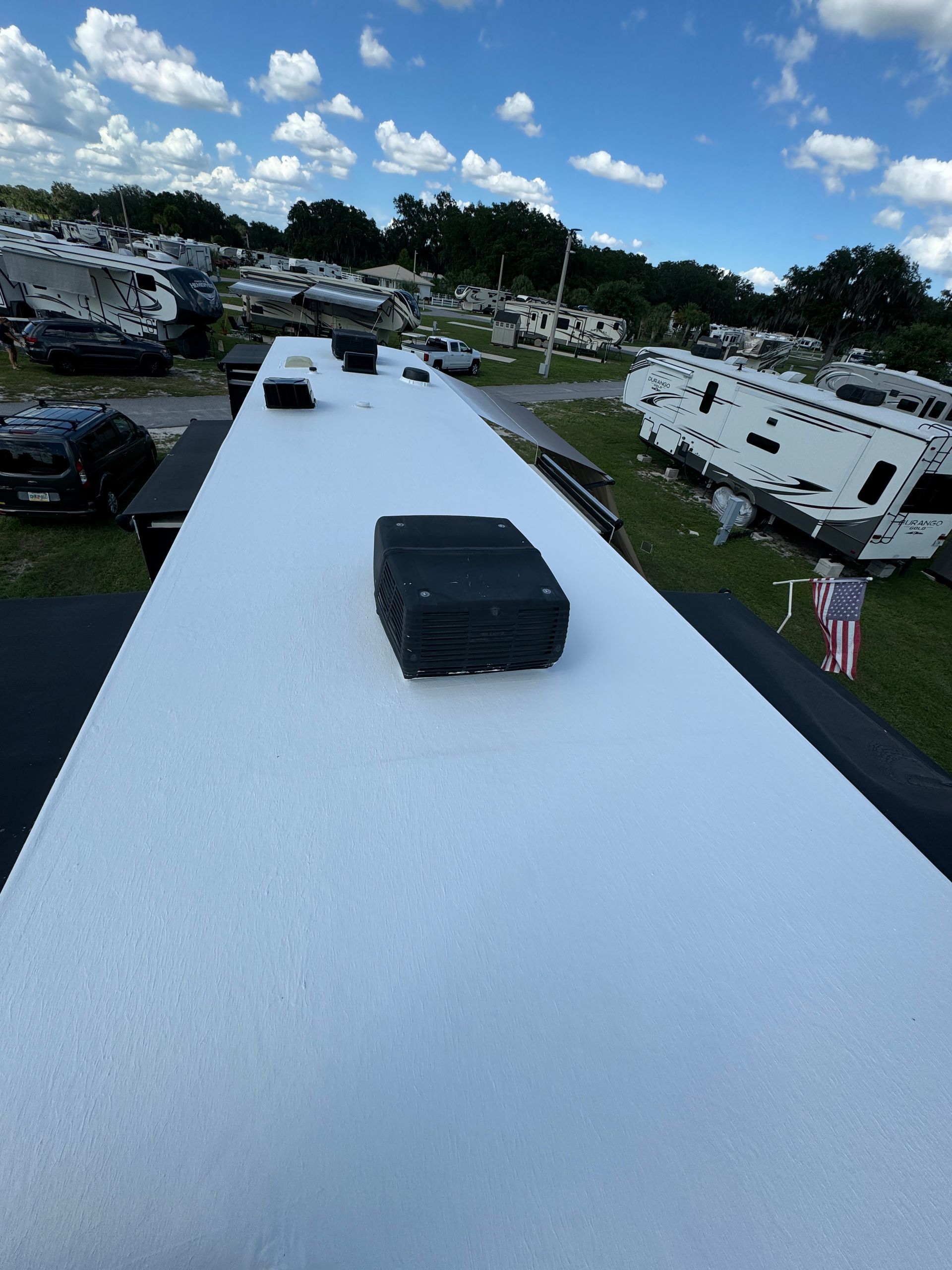 View from an RV roof with a black vent, overlooking a campground under a blue sky