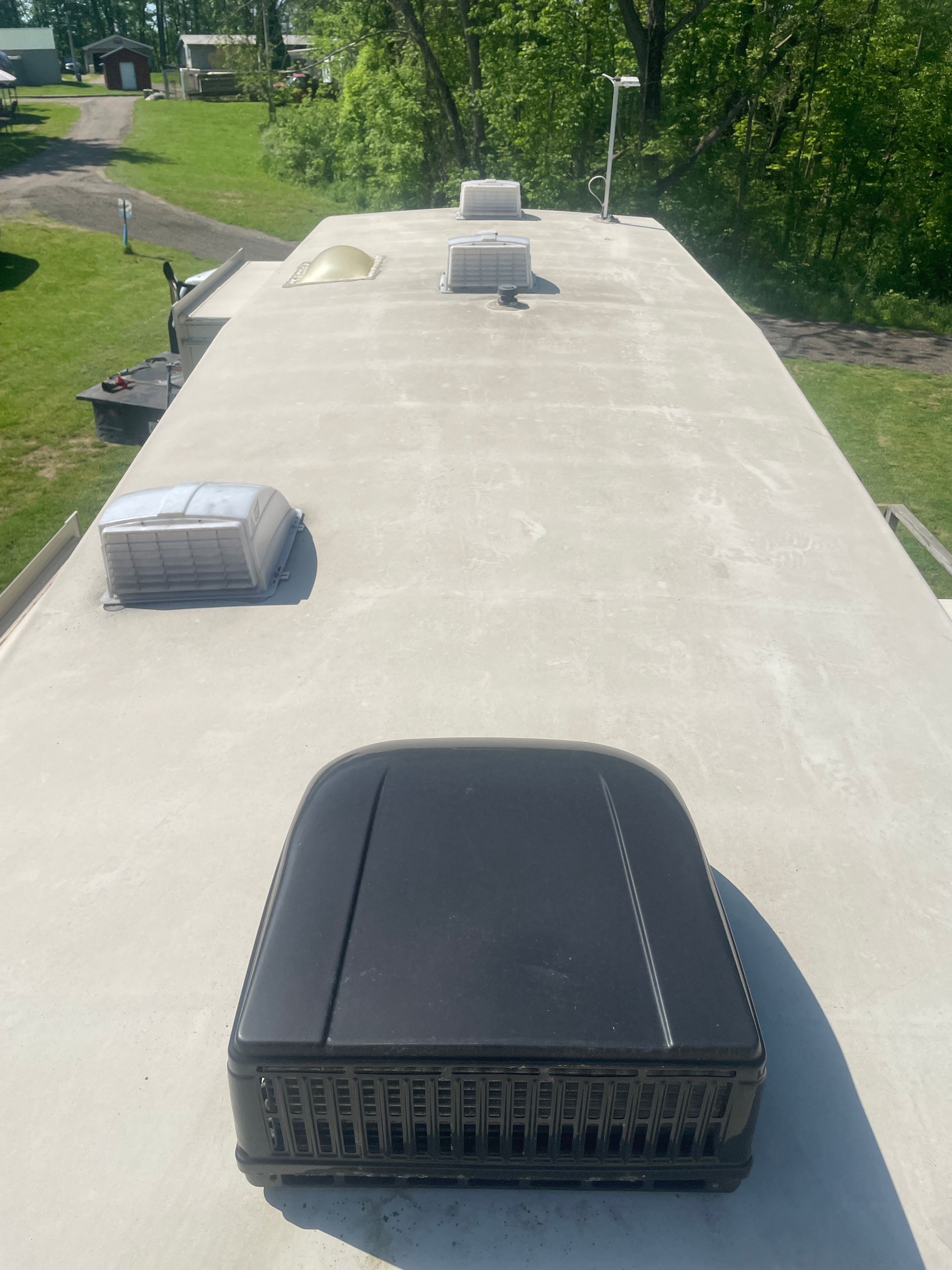RV roof with air conditioning unit, vents, and a clear sky in the background. White roof contrasts with the black A/C unit.