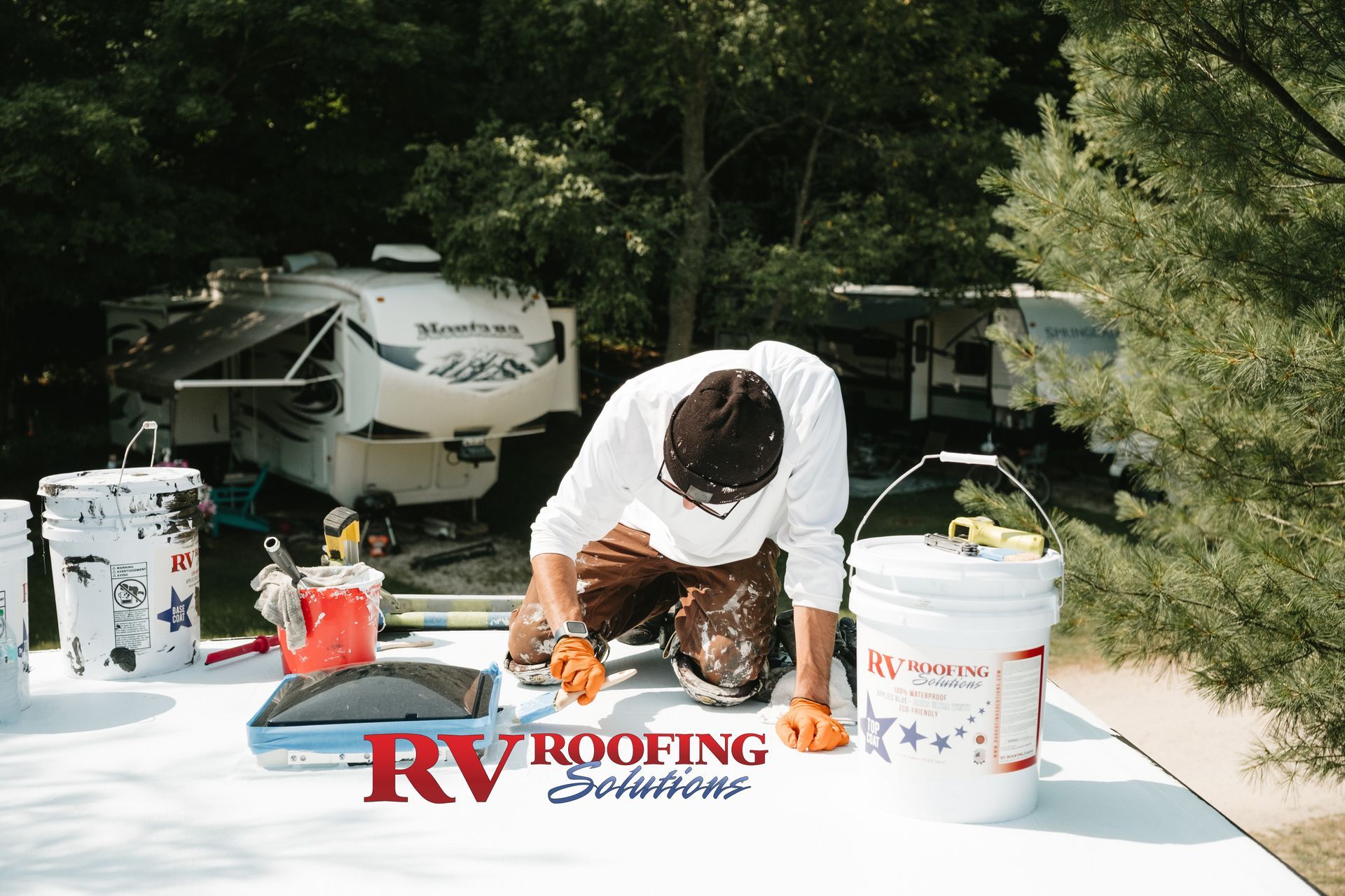 A person working on an RV roof; tools and buckets are in view, a white surface is being coated.