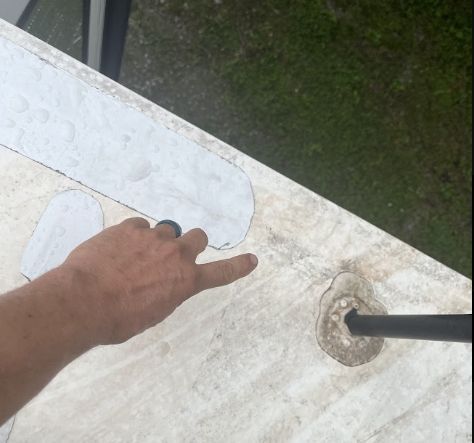 Hand pointing at a wet rv roof with tape on surface beside a rv roof ladder and patch of grass.