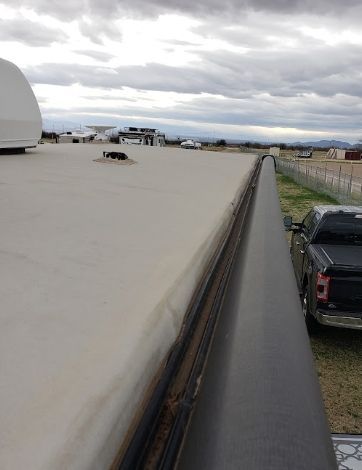 RV Rooftop edge with gutter and parked trucks beside a gravel lot under cloudy sky