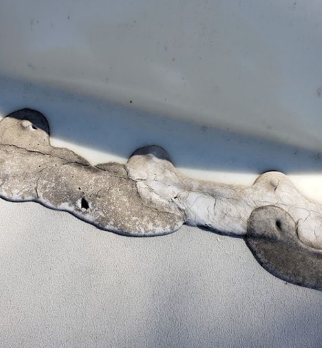 Close-up of cracked white caulk or sealant along a metal seam with dark gaps.