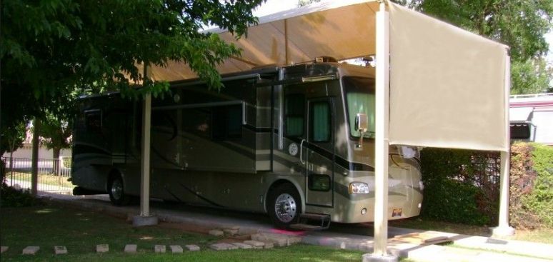 Motorhome parked under a carport beside trees and shrubs