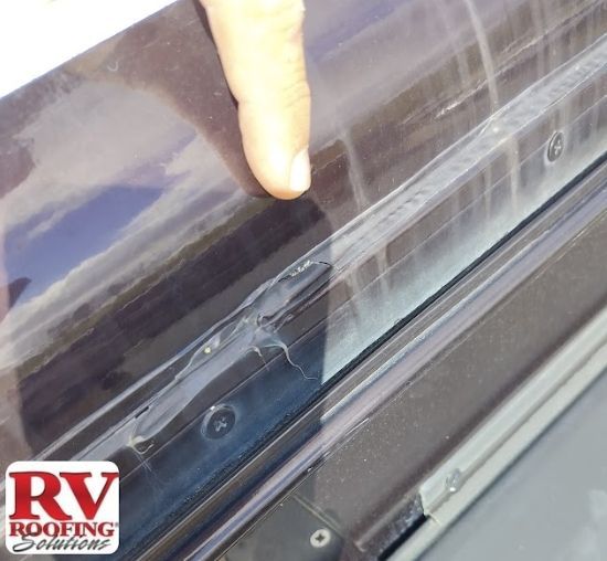Close-up of a finger pointing at a damaged RV skylight seal. The seal is cracked and peeling.