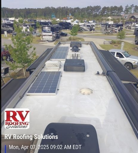 RV roof with solar panels and vents at a campground, viewed from the rear of the vehicle