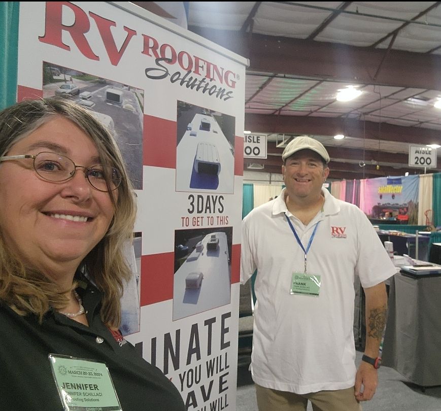 Two people smiling next to an RV Roofing Solutions banner at an event.
