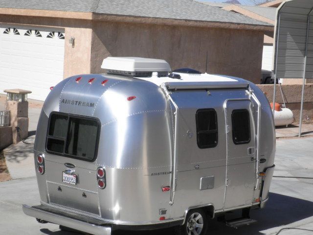 A silver airstream trailer is parked in front of a house