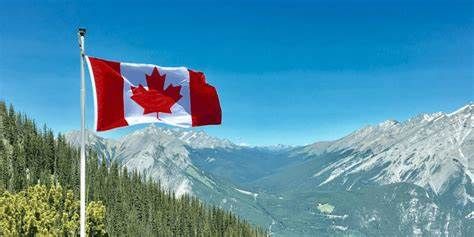 A canadian flag is flying in front of a mountain range.