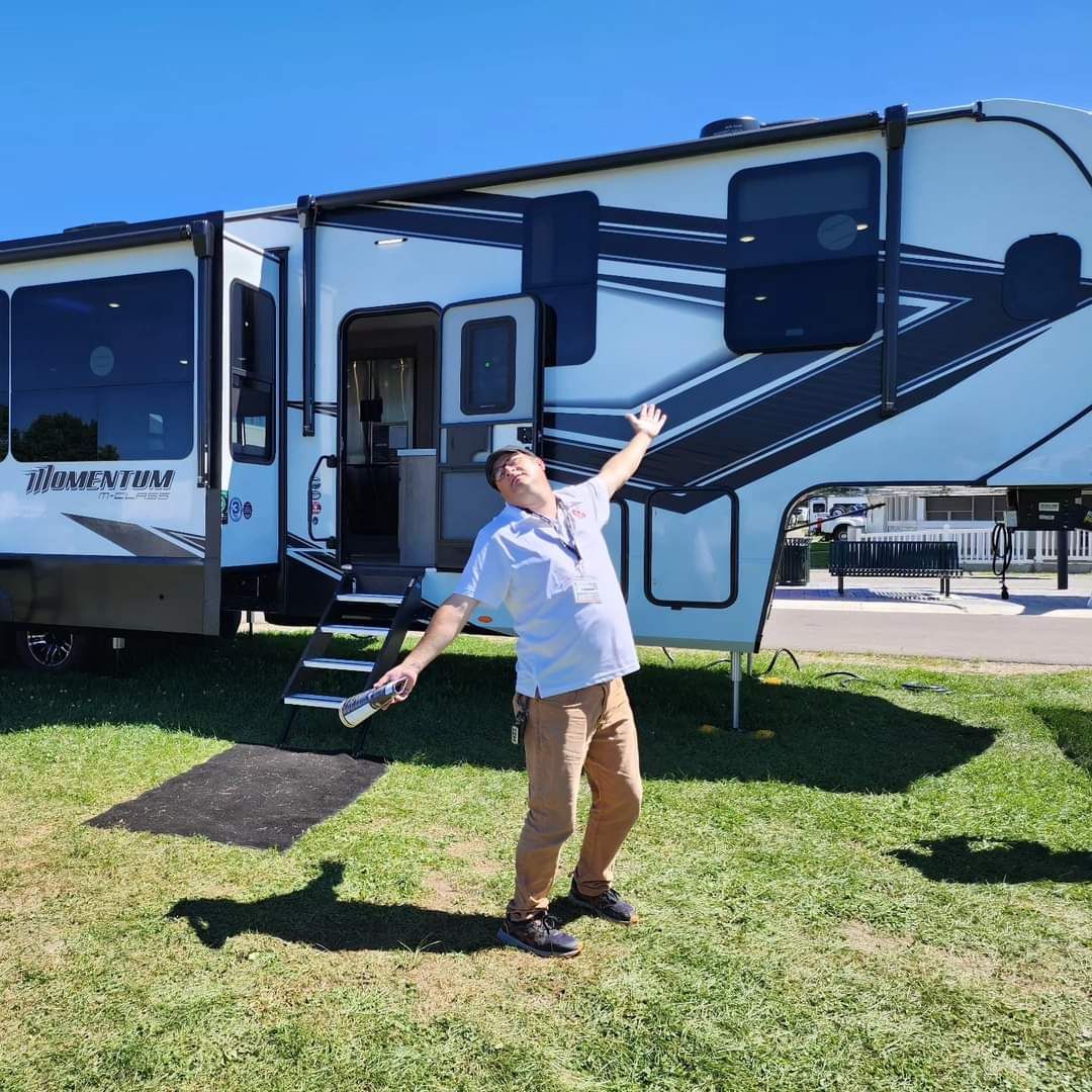 A man is standing in front of a rv with his arms outstretched.