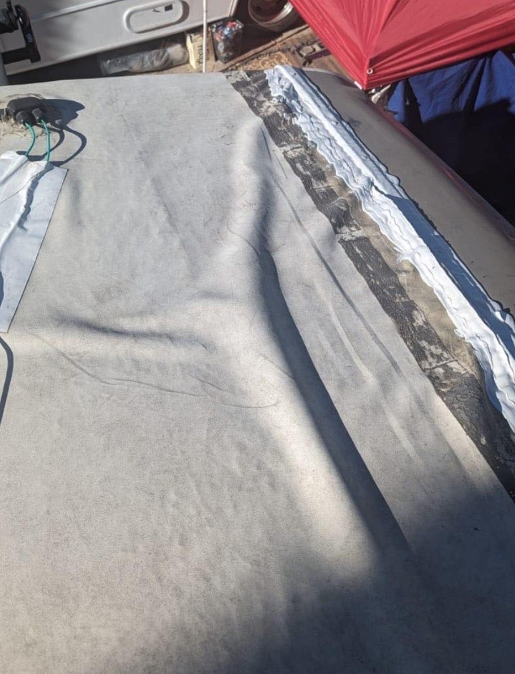 RV roof with torn membrane and exposed edges, a dark gray roof with light gray material laid over it.