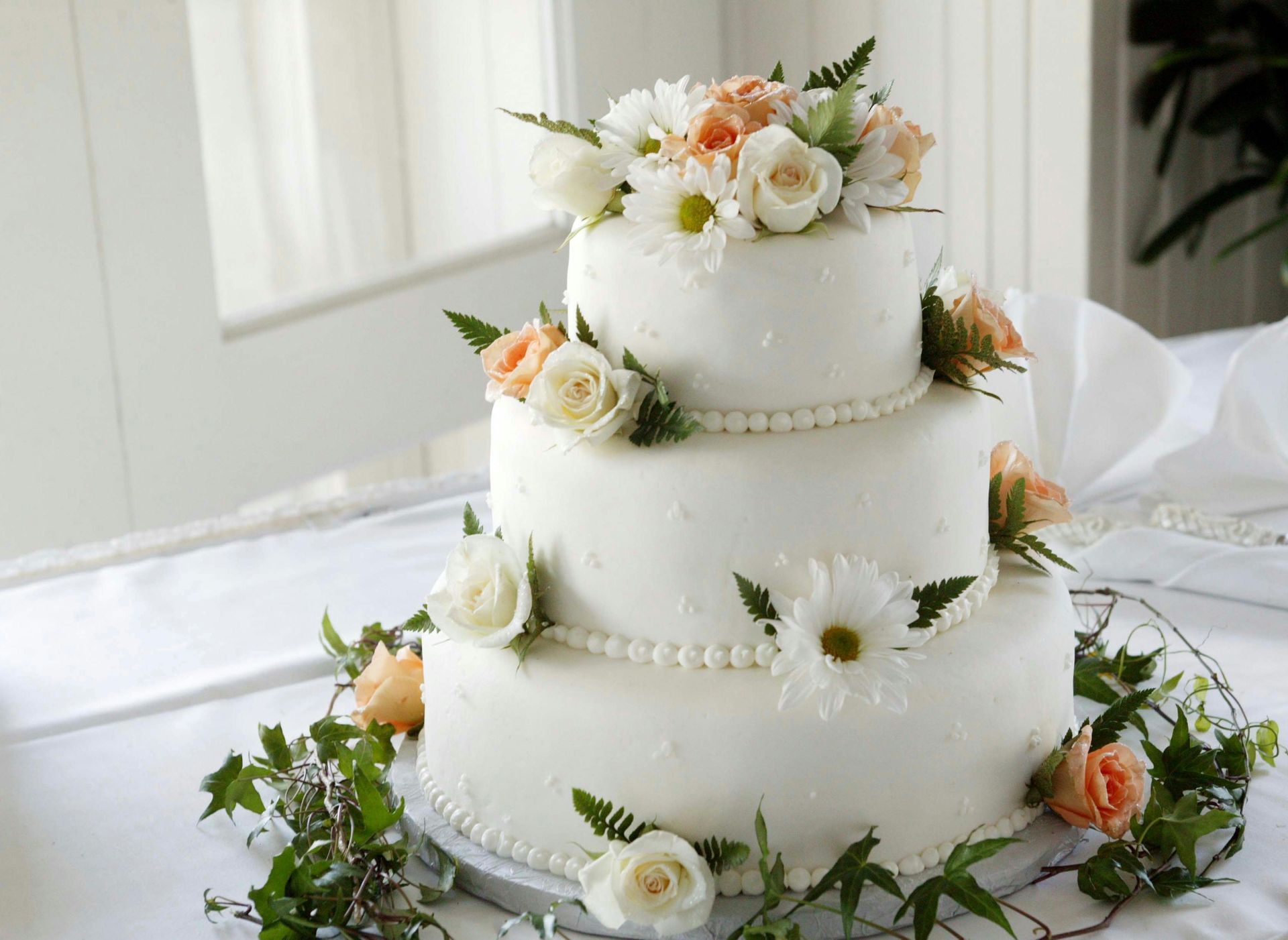 A three tiered wedding cake decorated with flowers and pearls on a table.