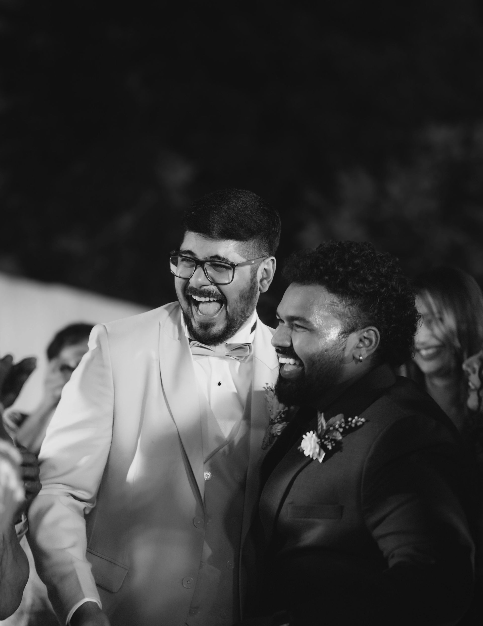 Two men in suits are laughing together in a black and white photo.