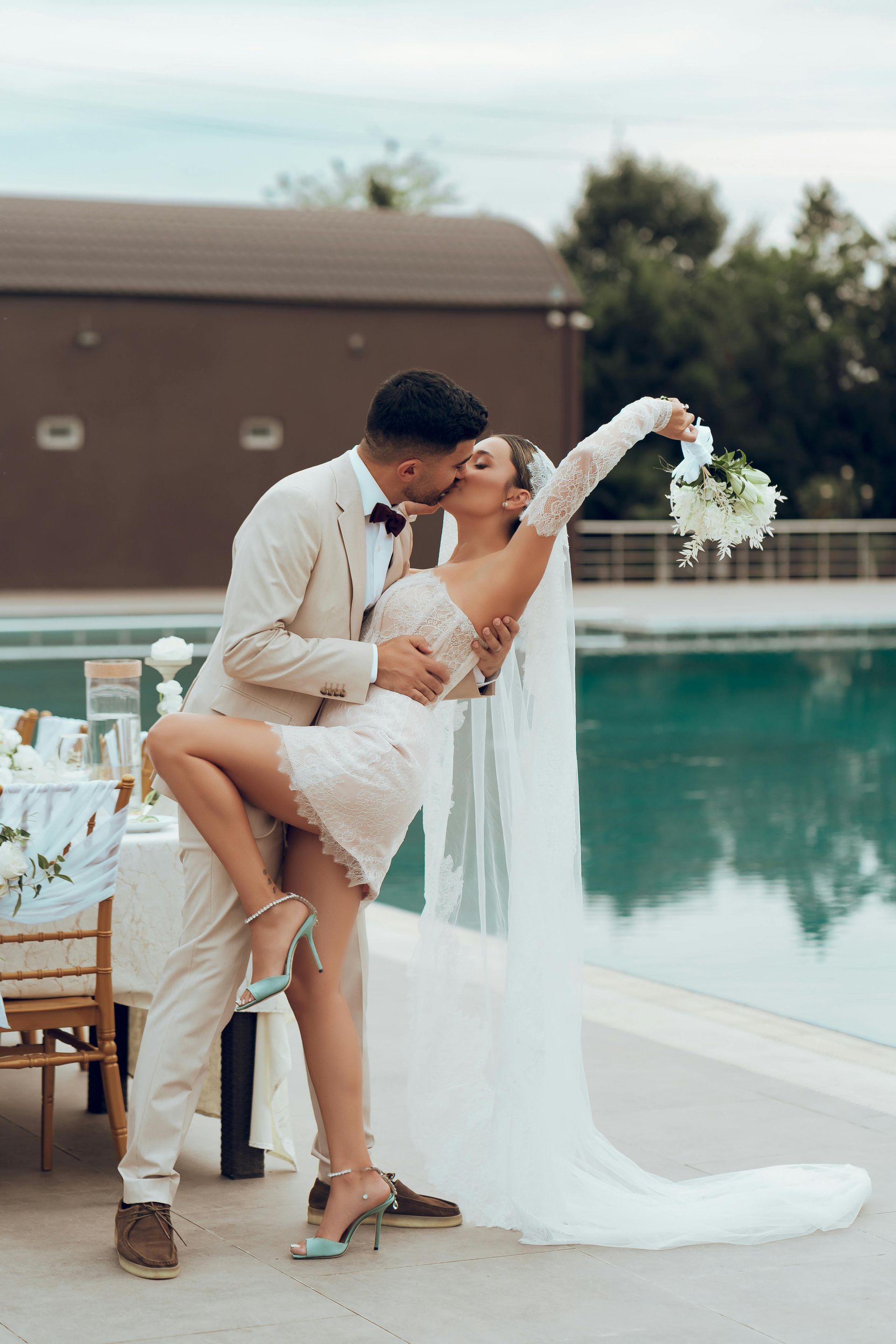 A bride and groom are kissing in front of a swimming pool.