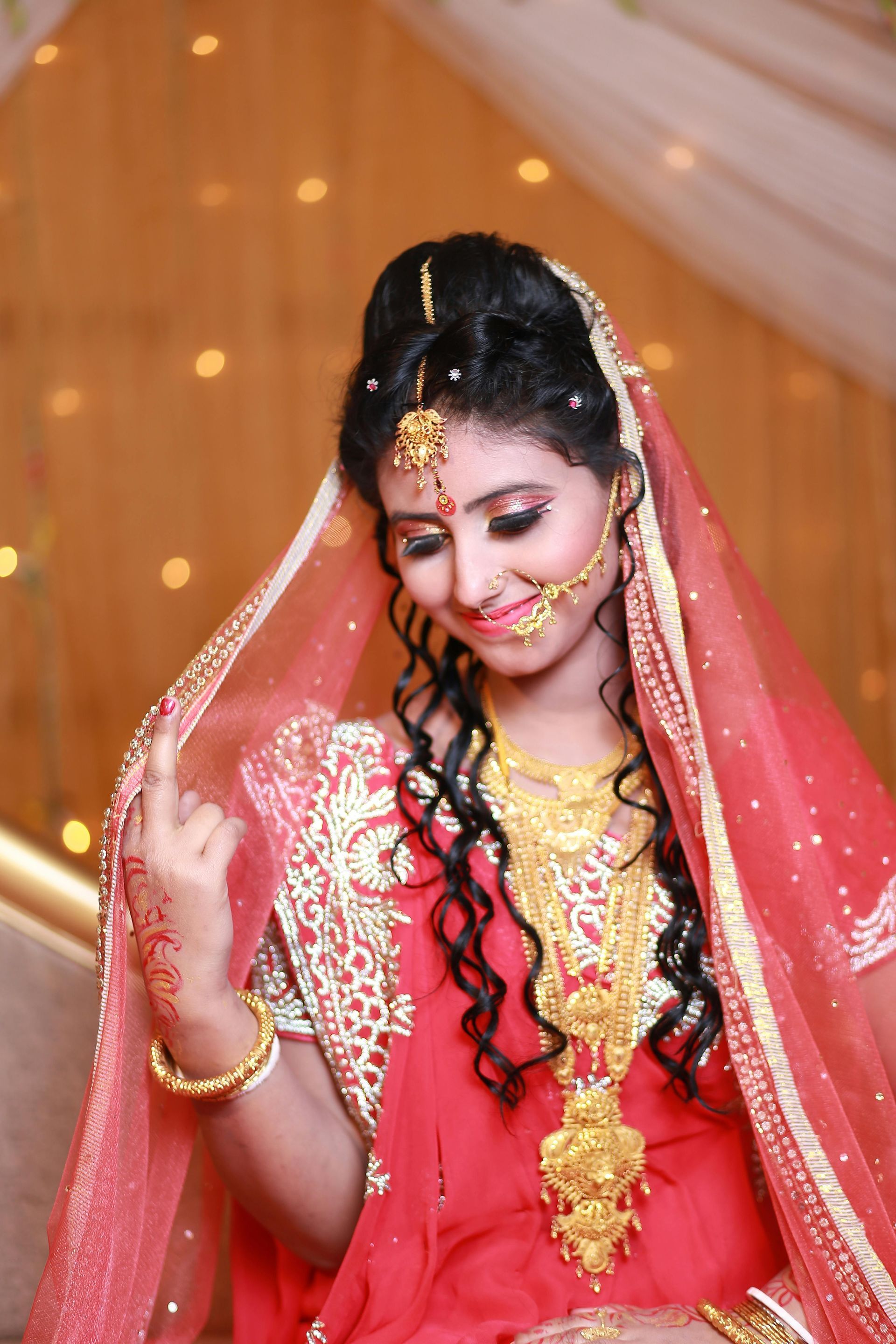 A bride in a red dress and gold jewelry is sitting on a couch.