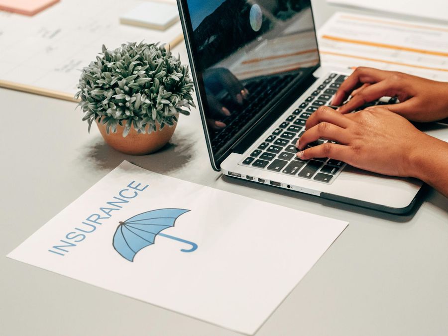 Person typing on laptop near an "Insurance" document with an umbrella icon.