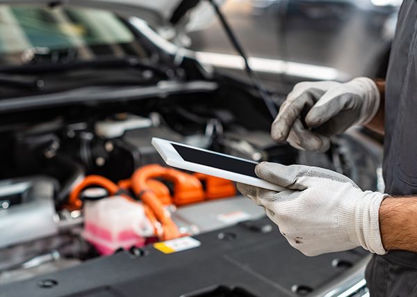 A man is holding a tablet in front of a car engine.