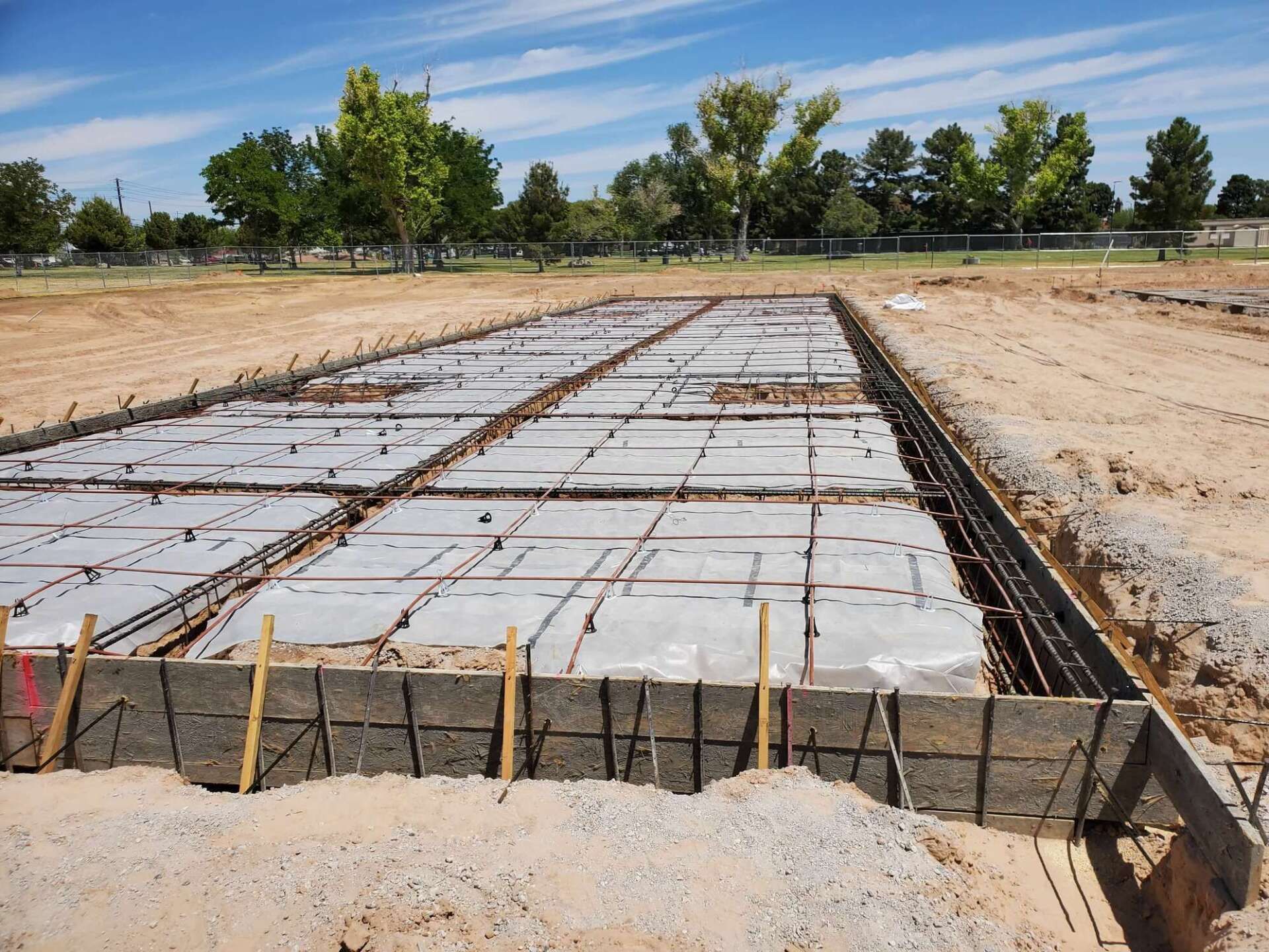 Concrete foundation under construction, with rebar and wooden forms in a dirt field.