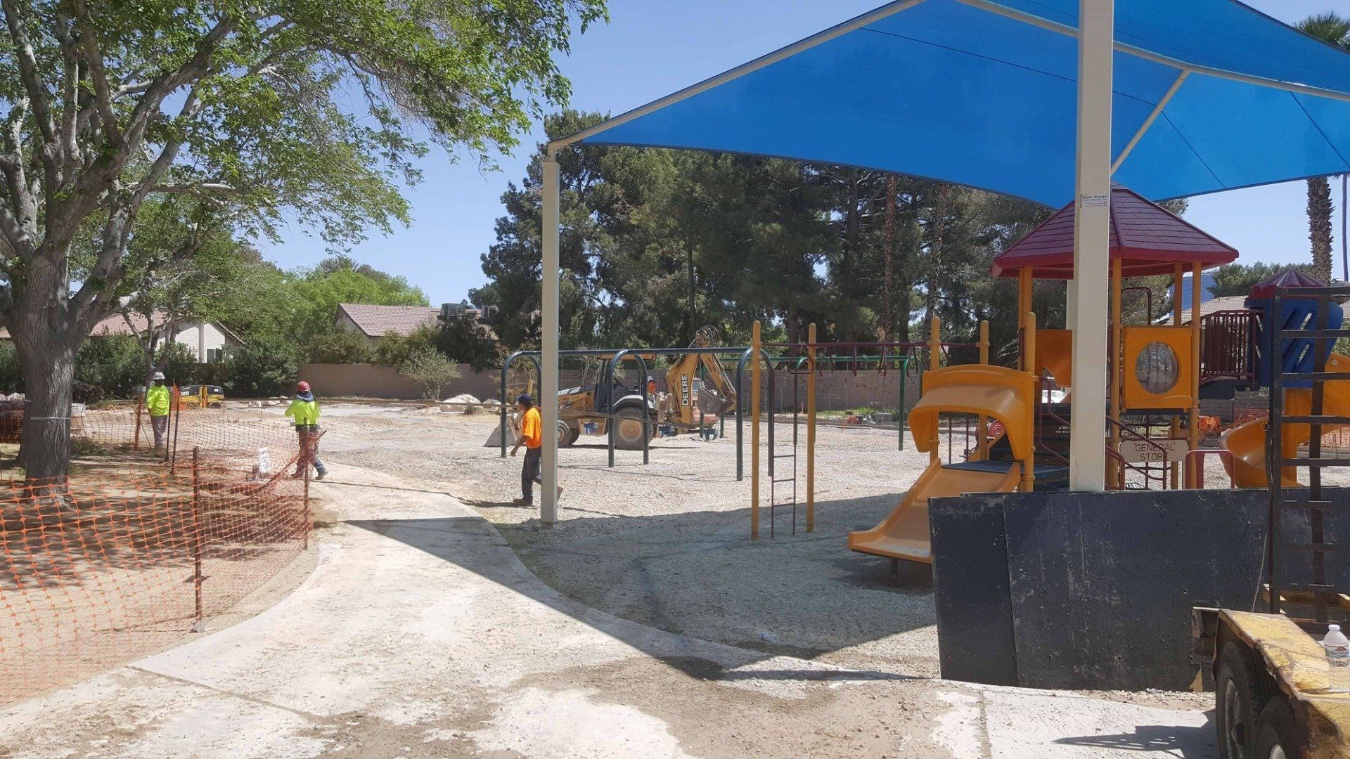 Playground under construction; workers, equipment, and blue shade structure.